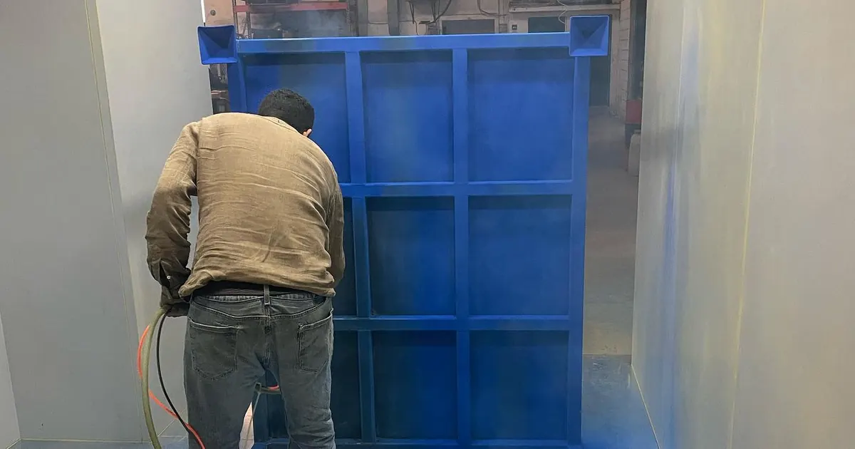 Operador aplicando pintura electrostática en polvo azul sobre una estructura metálica dentro de cabina en Steel Paint