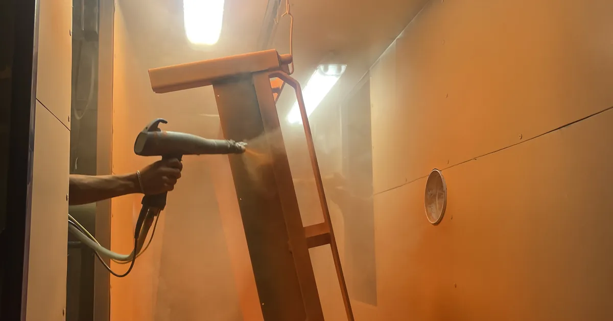 Aplicación de pintura electrostática en polvo con pistola sobre una pieza metálica dentro de cabina en Steel Paint