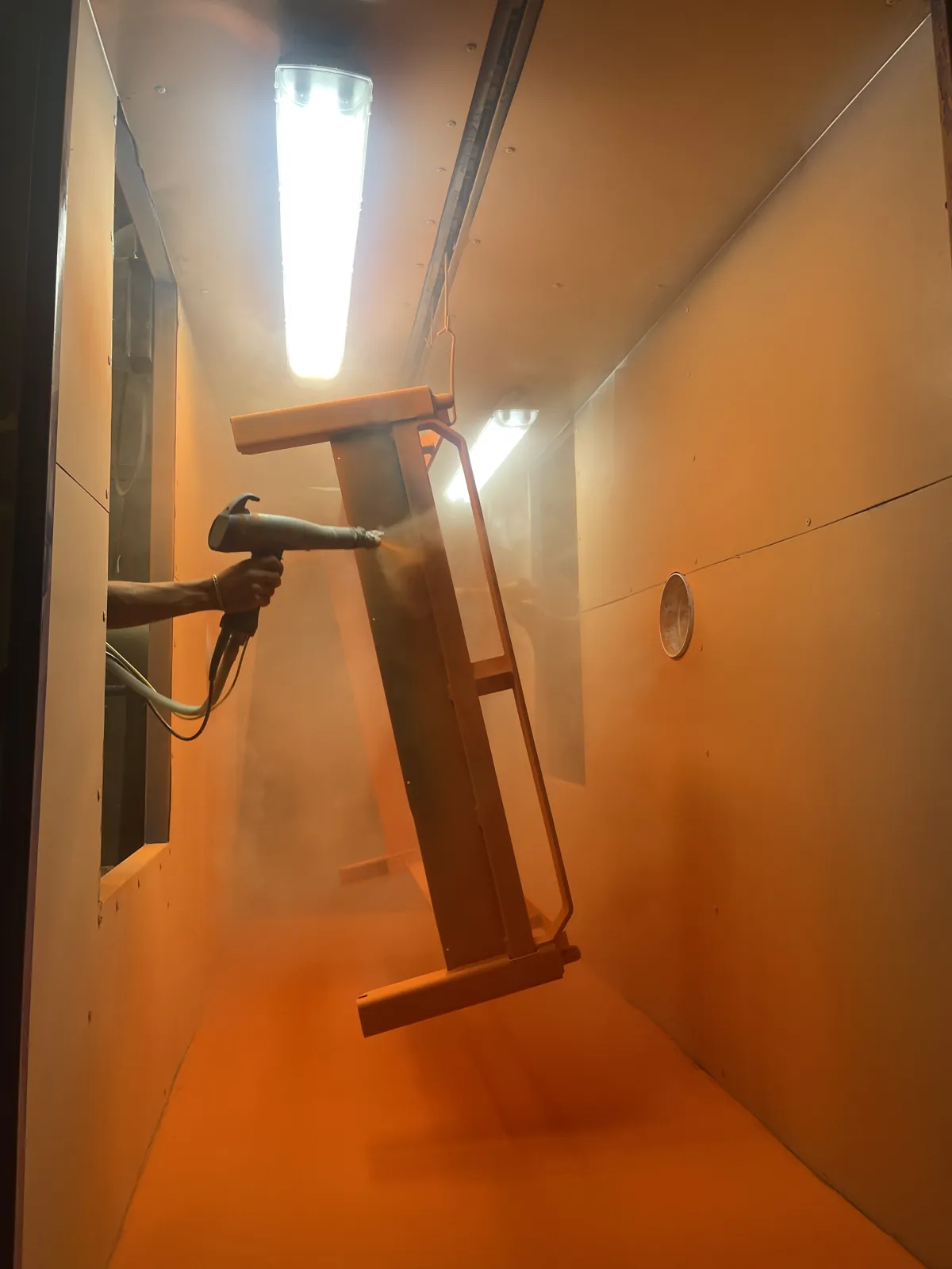 Aplicación de pintura electrostática en polvo con pistola sobre una pieza metálica dentro de cabina en Steel Paint